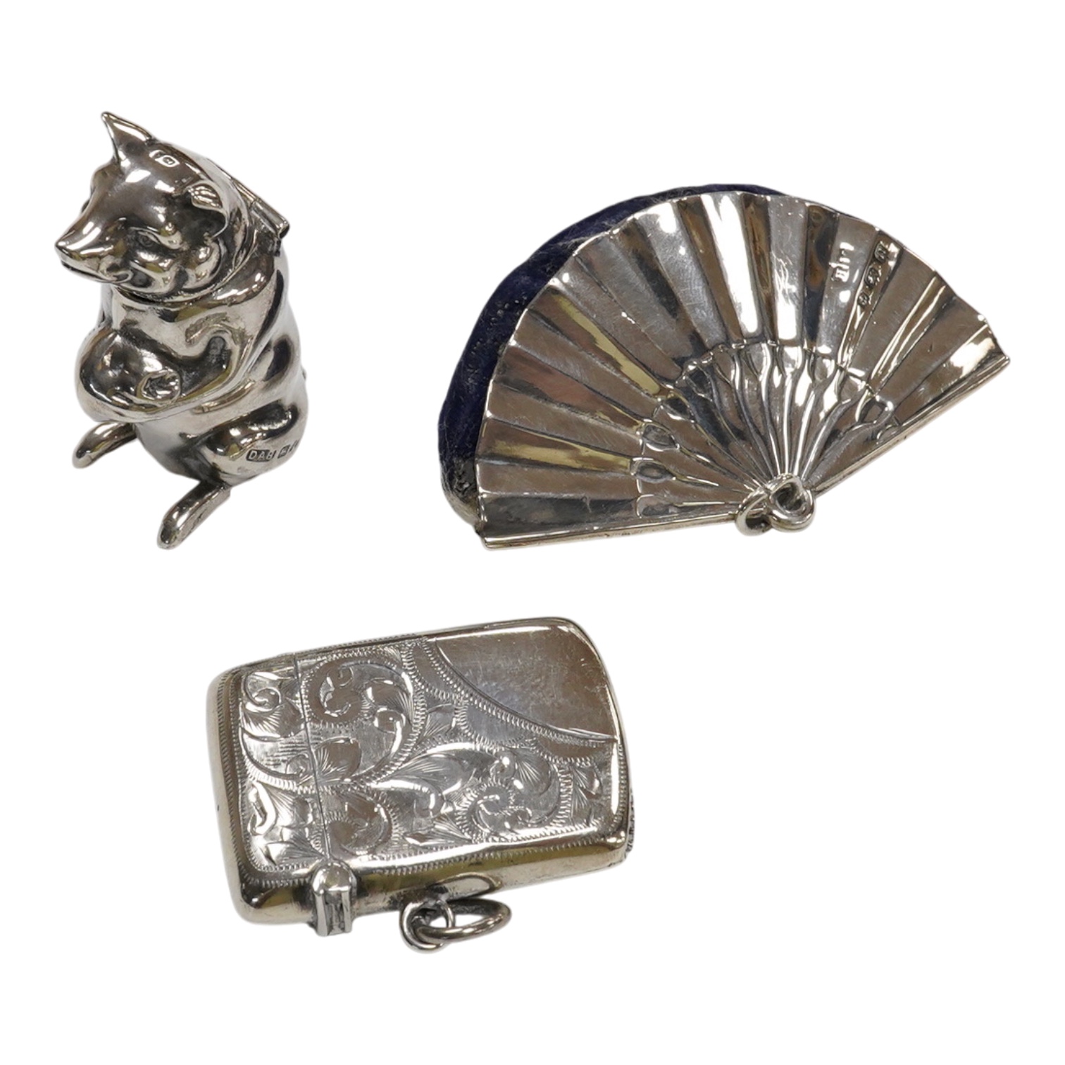 A George V silver mounted fan pin cushion, Henry Matthews, Birmingham, 1912, width 62mm, together with an Edwardian silver vesta case and a white metal pig vesta case.